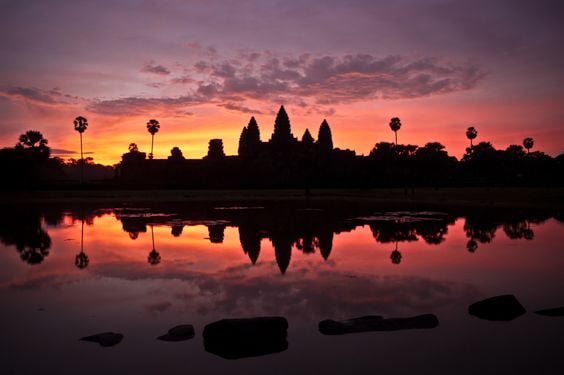 Silhouette of Angkor Wat's five lotus towers reflected in water at dawn, Cambodia.