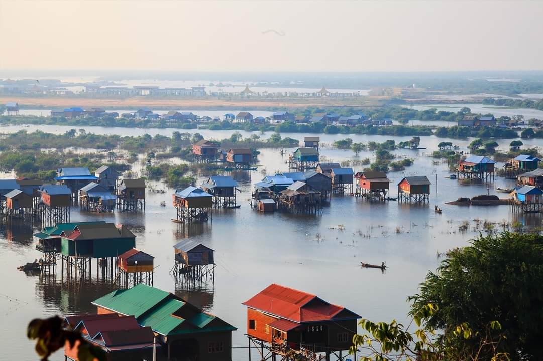 Floating village on Tonle Sap Lake, wooden houses and boats on brown water amidst flooded trees-03